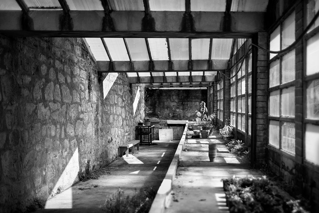 A glazed corridor with shadows and objects at the far end.